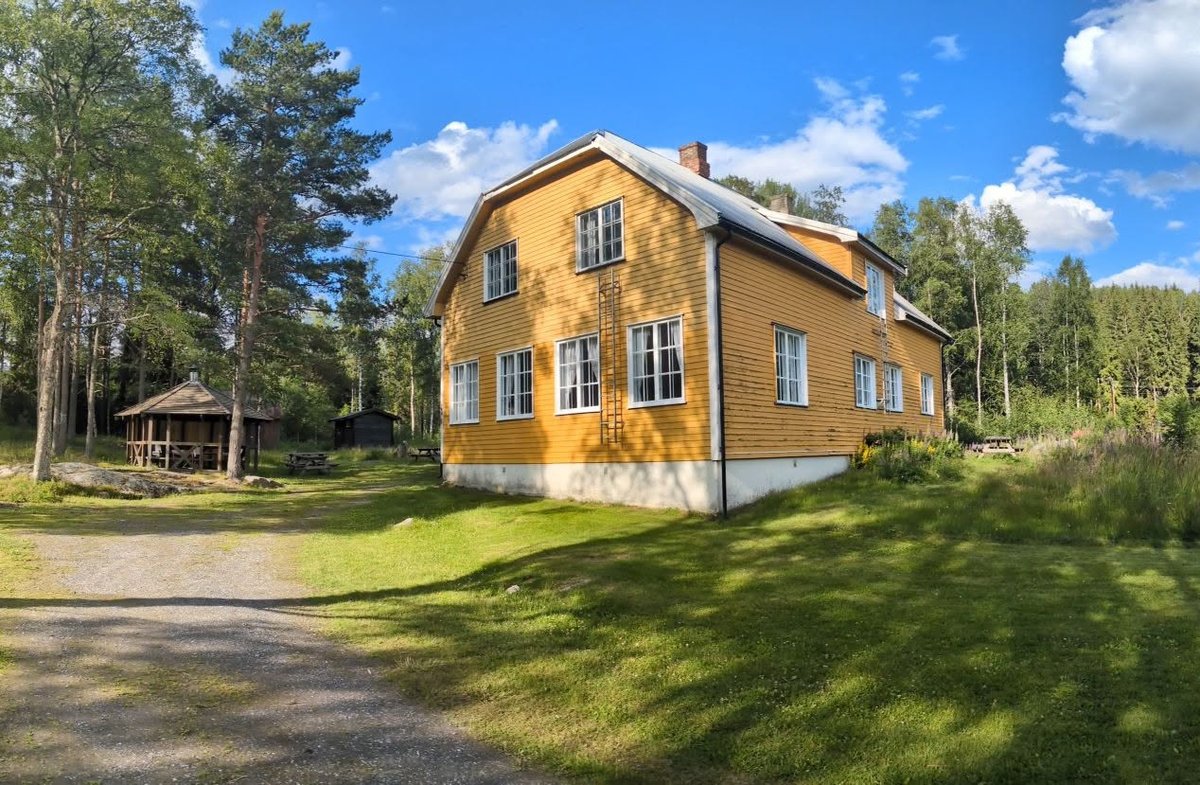 Bjørknes gamle skole, et gult skolehus i tre med store vinduer, omgitt av skog.